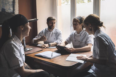 Männliche und weibliche Köche diskutieren, während sie am Tisch im Restaurant sitzen - MASF20127