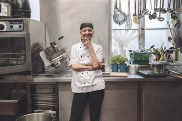 Porträt eines glücklichen reifen Kochs mit Hand am Kinn in einer Großküche - MASF20131