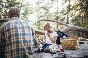 Tochter isst Wassermelone, während sie mit ihrem Vater auf einer Picknickdecke im Wald sitzt - MASF20173