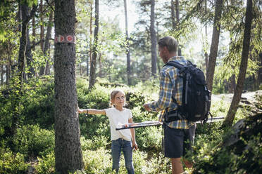 Tochter im Gespräch mit dem Vater, während sie an einem Baumstamm im Wald steht - MASF20178