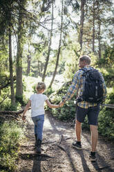 Rear view of daughter holding hands with father while walking in forest - MASF20181