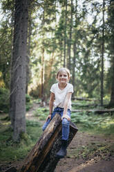 Portrait of smiling daughter sitting on log in forest - MASF20187