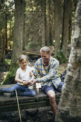 Lächelnder Vater hilft seiner Tochter beim Schneiden auf einem Steg im Wald - MASF20194