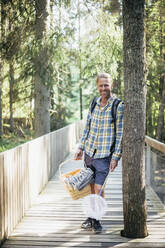 Porträt eines lächelnden Mannes mit Picknickkorb auf einem Steg im Wald - MASF20195