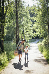 Tochter spricht mit Vater, der einen Picknickkorb auf einer Straße im Wald hält - MASF20202