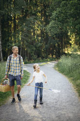 Smiling daughter talking to father holding picnic basket on road in forest - MASF20203