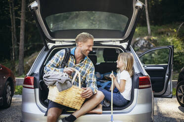 Lächelnder Vater mit Picknickkorb im Gespräch mit seiner Tochter, während er im Kofferraum eines Autos sitzt - MASF20205