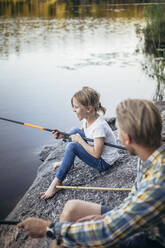 Smiling daughter enjoying fishing with father at lake - MASF20217