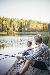 Smiling daughter looking at father while fishing at lake - MASF20218