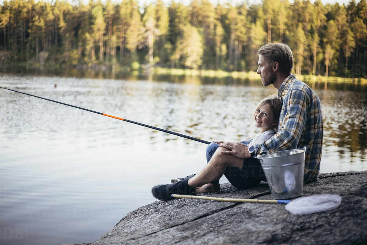 Portrait of smiling daughter fishing with father while sitting by lake  stock photo