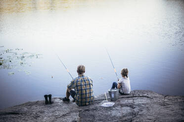 Rear view of father and daughter fishing at lake - MASF20221