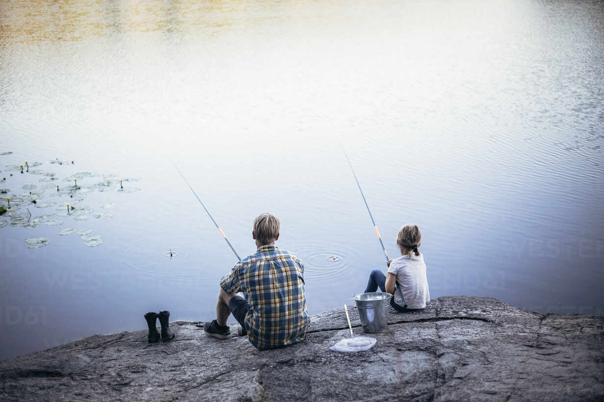 Rear view of father and daughter fishing at lake stock photo