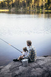 Father and daughter fishing while sitting by lake - MASF20222