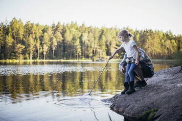 Father holding daughter during fishing while crouching by lake - MASF20225