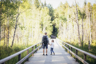 Vater mit Rucksack im Gespräch mit Tochter auf einem Steg im Wald - MASF20226