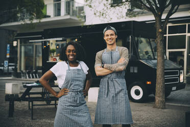 Portrait of smiling male and female owners standing against food truck in city - MASF20238