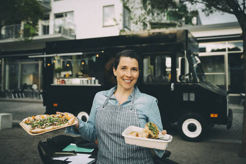 Portrait of smiling female owner with indian street food against commercial land vehicle stock photo