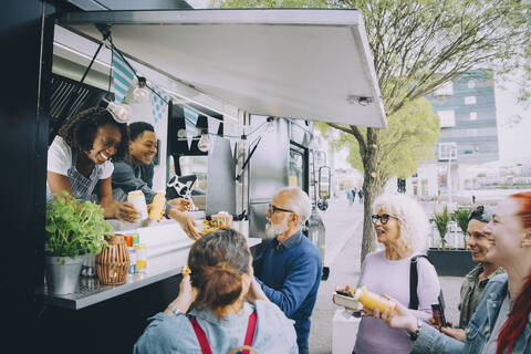 Smiling male and female customers talking to food truck owners in city stock photo
