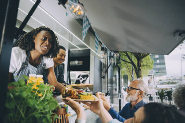 Lächelnde Besitzer, die den Kunden indisches Essen geben, während sie in einem kommerziellen Landfahrzeug stehen - MASF20255