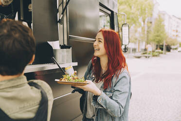 Lächelnde Kundin im Gespräch mit dem Besitzer, während sie mit einem Teller Essen auf der Straße steht - MASF20292