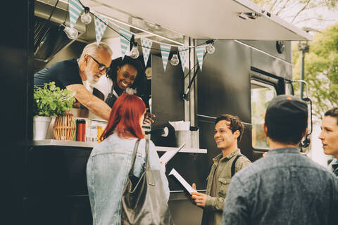 Owner with assistant talking to smiling customers by food truck stock photo