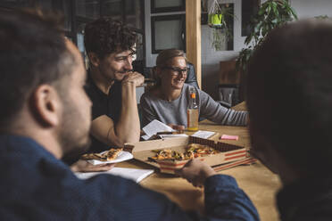 Smiling coworkers eating pizza at workplace - MASF20306