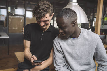 Smiling businessman showing mobile phone to coworker at workplace - MASF20311