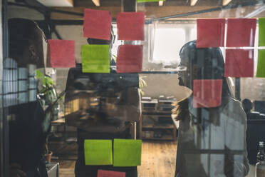 Male an female coworkers discussing over sticky notes seen through glass door - MASF20327