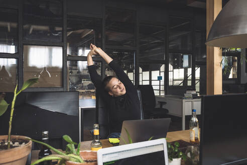 Freelancer stretching by desk at workplace - MASF20344