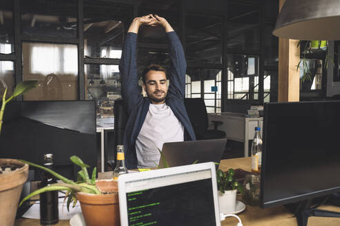 Freelancer stretching while looking at laptop by desk - MASF20347