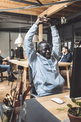 Smiling computer programmer stretching at workplace - MASF20369