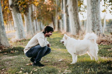 Man talking with dog while crouching at forest - EBBF01027