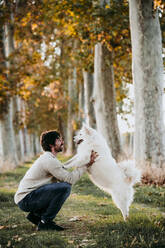 Man playing with dog while crouching at forest - EBBF01028