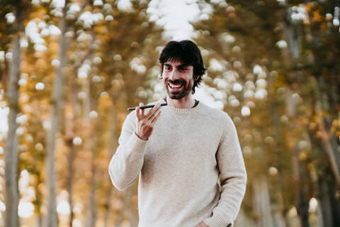 Smiling man talking on mobile phone while walking at forest stock photo
