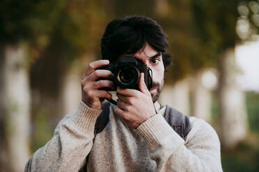 Mid adult man taking photo with camera while standing at forest - EBBF01043