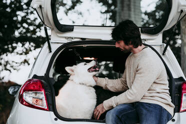 Mann sitzt mit Hund im Kofferraum eines Autos im Wald - EBBF01046