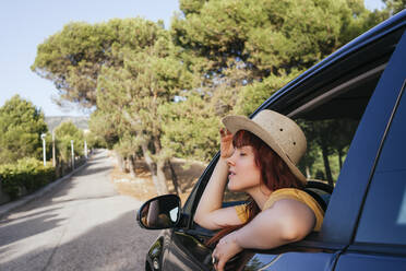 Young redhead woman leaning out from car window - MGRF00005