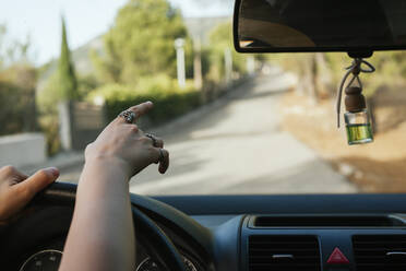Hand einer jungen Frau, die aus dem Autoinneren auf die Straße zeigt - MGRF00006