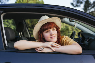 Smiling young beautiful redhead woman leaning out from car window - MGRF00007