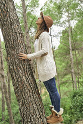 Frau berührt sich, während sie zu einem Baumstamm im Wald hinaufschaut - VEGF03000