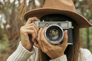 Woman photographing through vintage camera in forest - VEGF03009