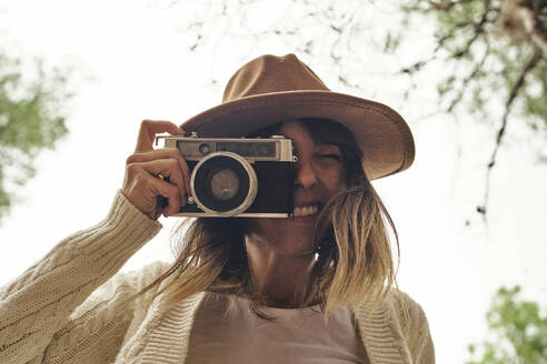 Lächelnde Frau, die durch eine alte Kamera im Wald fotografiert - VEGF03010