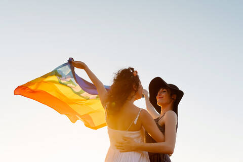 Happy women raising multicolored flag standing on sea beach stock photo