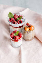 Composition of delicious puddings made from chia seeds yogurt topped with raspberry jam and cherry in glass jars on grey table - ADSF16965