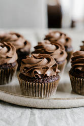 Appetitliche süße Schokoladen-Cupcakes mit Schokoladenbuttercreme, serviert auf einem runden Tablett auf dem Tisch - ADSF16966