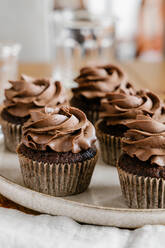 Appetitliche süße Schokoladen-Cupcakes mit Schokoladenbuttercreme, serviert auf einem runden Tablett auf dem Tisch - ADSF16967