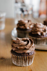 Appetitliche süße Schokoladen-Cupcakes mit Schokoladenbuttercreme, serviert auf einem runden Tablett auf dem Tisch - ADSF16968