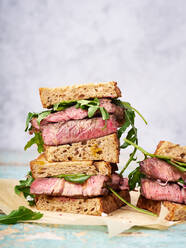 Nahaufnahme eines Stapels von Rindersteak-Sandwich mit Rucola und Senf-Dressing gegen hellen Hintergrund - ADSF16982