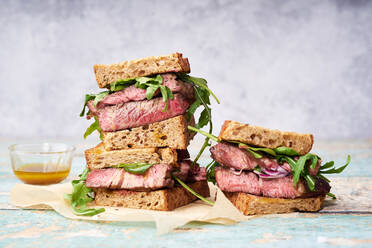 Nahaufnahme eines Stapels von Rindersteak-Sandwich mit Rucola und Senf-Dressing gegen hellen Hintergrund - ADSF16983