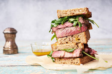 Nahaufnahme eines Stapels von Rindersteak-Sandwich mit Rucola und Senf-Dressing gegen hellen Hintergrund - ADSF16984
